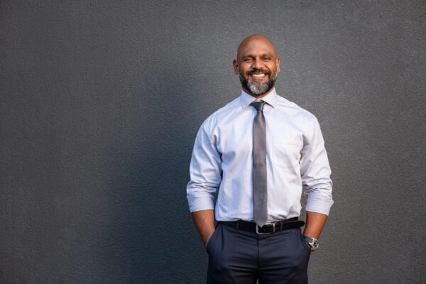 Portrait,Of,Successful,Black,Businessman,Standing,Against,Grey,Wall.,Smilng