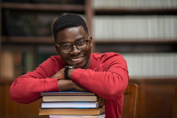 Portrait,Of,Happy,African,Student,Wearing,Spectacles,Sitting,In,Library