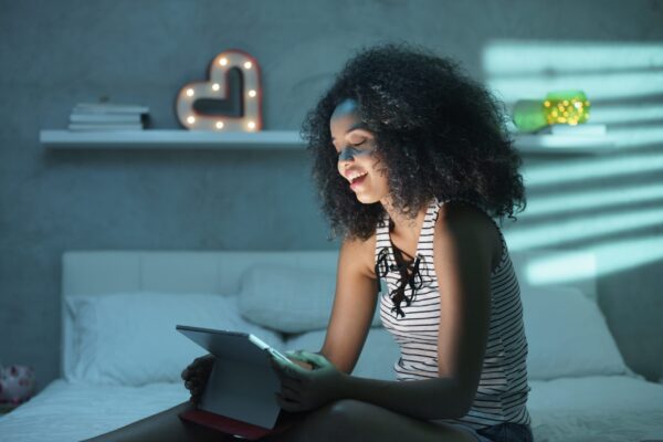 Happy,African,American,Teenager,In,Bed,At,Home,With,Tablet.