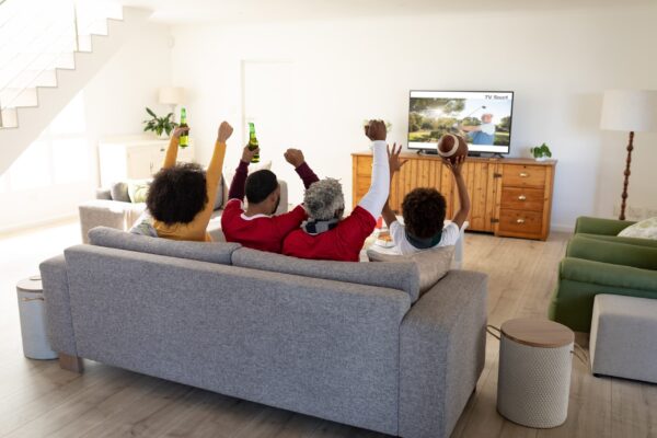 Rear,View,Of,Family,Sitting,At,Home,Together,Watching,Golf